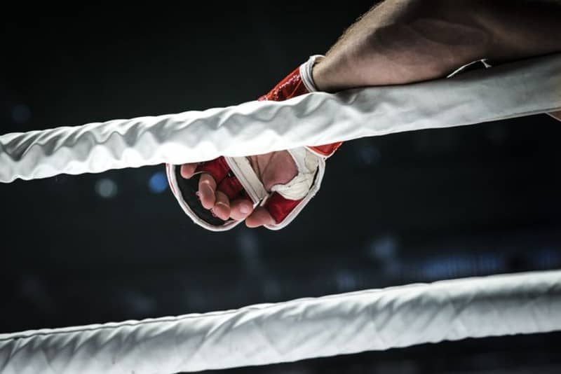 closeup hand of fighter MMA in glove lays ropes of ring